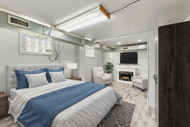 bedroom with concrete block wall, light wood-style floors, a fireplace, and visible vents