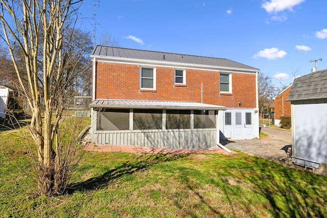 back of property featuring a sunroom, a yard, metal roof, and brick siding