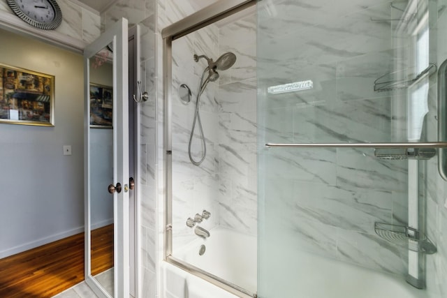 bathroom featuring baseboards, bath / shower combo with glass door, and wood finished floors