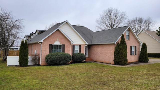 view of front of property featuring a shingled roof, fence, a front lawn, and brick siding