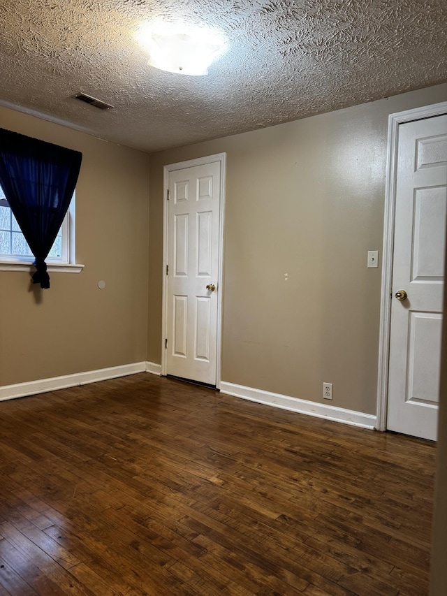 empty room featuring a textured ceiling, dark wood-type flooring, visible vents, and baseboards