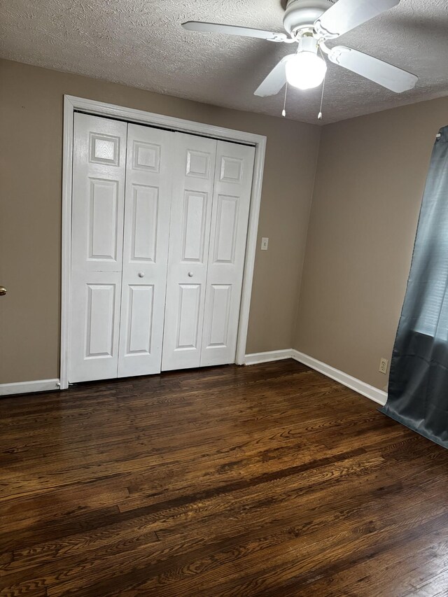 unfurnished bedroom with dark wood finished floors, a closet, ceiling fan, a textured ceiling, and baseboards