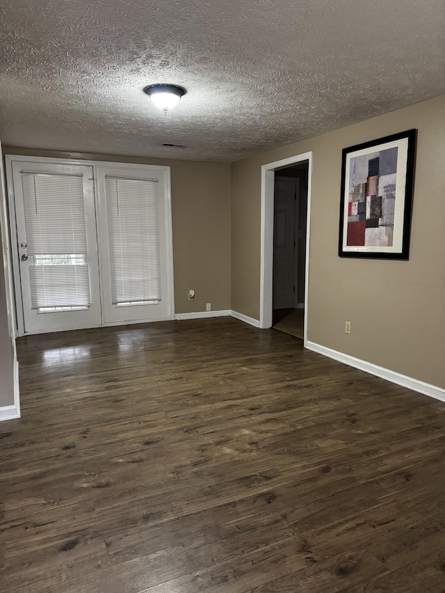 empty room featuring a textured ceiling, dark wood finished floors, and baseboards