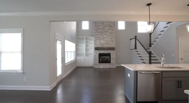 unfurnished living room featuring crown molding, stairway, a sink, a stone fireplace, and baseboards