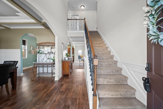 foyer featuring dark wood-style floors, stairs, arched walkways, and wainscoting