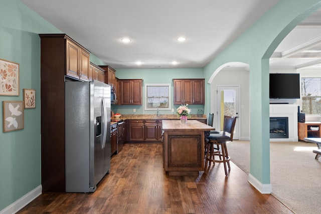 kitchen featuring a breakfast bar area, stainless steel appliances, a kitchen island, open floor plan, and dark wood finished floors