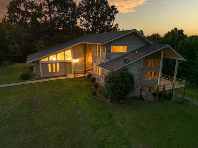 back of house at dusk featuring stone siding and a yard