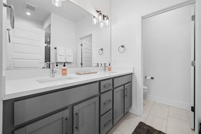 bathroom with visible vents, double vanity, a sink, and toilet