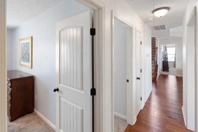 hall with baseboards, visible vents, a textured ceiling, and wood finished floors