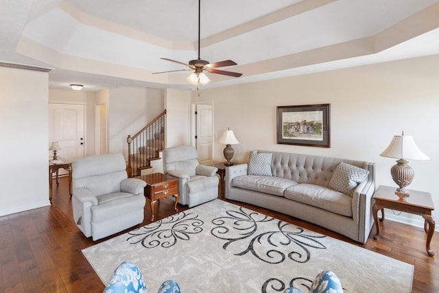 living area with baseboards, a raised ceiling, a ceiling fan, hardwood / wood-style flooring, and stairway