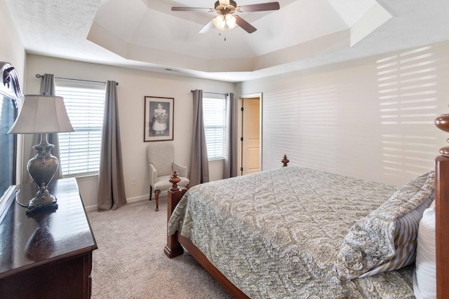 carpeted bedroom with a ceiling fan, a tray ceiling, multiple windows, and baseboards