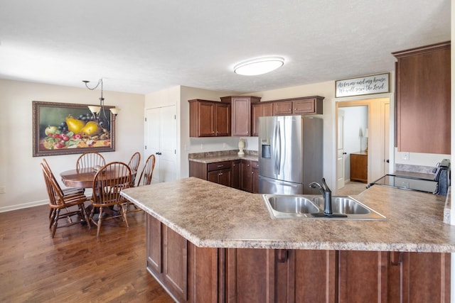 kitchen with a peninsula, dark wood-type flooring, a sink, light countertops, and stainless steel refrigerator with ice dispenser