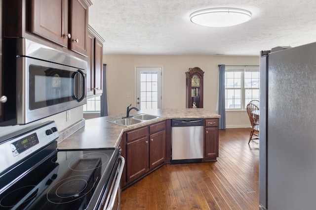 kitchen featuring a textured ceiling, stainless steel appliances, a peninsula, a sink, and dark wood finished floors