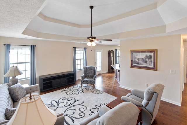 living room with dark wood-type flooring, a wealth of natural light, and a raised ceiling