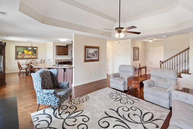 living room featuring a raised ceiling, dark wood finished floors, baseboards, and stairs