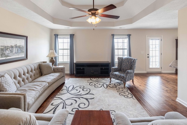 living room with a wealth of natural light, a raised ceiling, baseboards, and wood finished floors