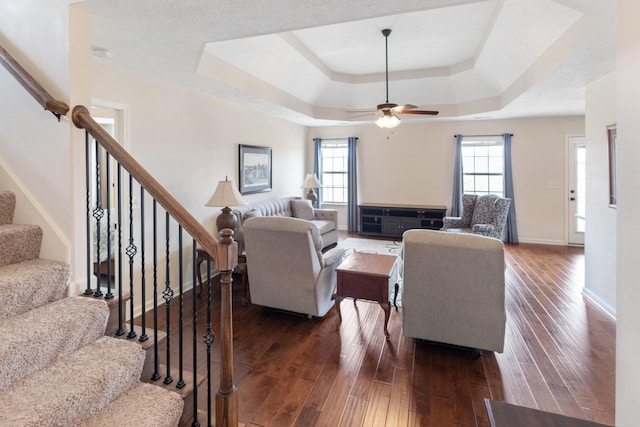 living area featuring stairway, baseboards, a tray ceiling, and dark wood finished floors