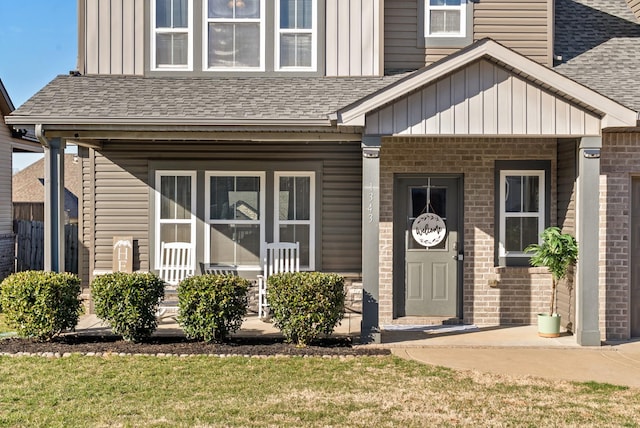 doorway to property with a shingled roof, covered porch, brick siding, and board and batten siding