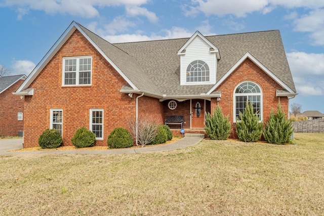 view of front of home with roof with shingles, brick siding, and a front lawn