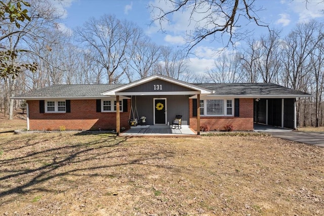 single story home featuring brick siding, concrete driveway, covered porch, a front yard, and a carport