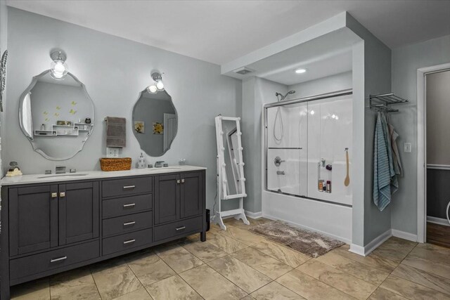 bathroom featuring combined bath / shower with glass door, a sink, baseboards, and double vanity