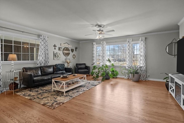 living room featuring ornamental molding, a ceiling fan, baseboards, and wood finished floors