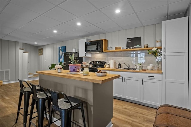 kitchen with visible vents, light wood-style floors, butcher block countertops, a breakfast bar area, and black appliances