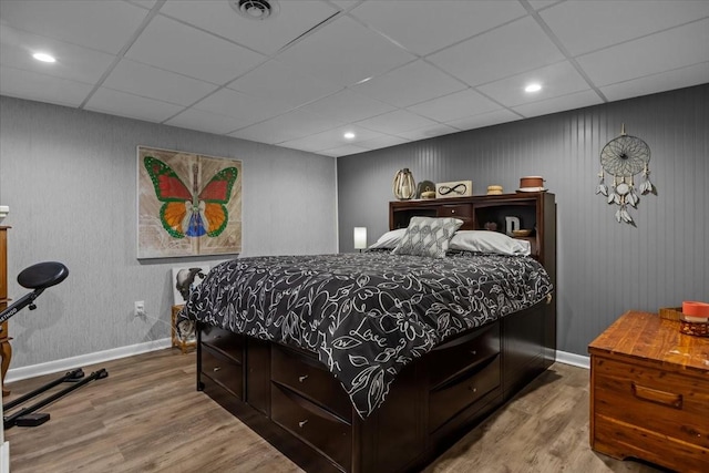 bedroom featuring a paneled ceiling, wood finished floors, visible vents, and baseboards