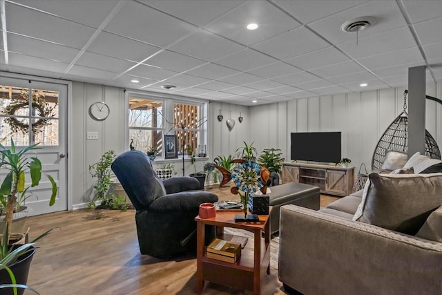 living area featuring a paneled ceiling, visible vents, a decorative wall, and wood finished floors