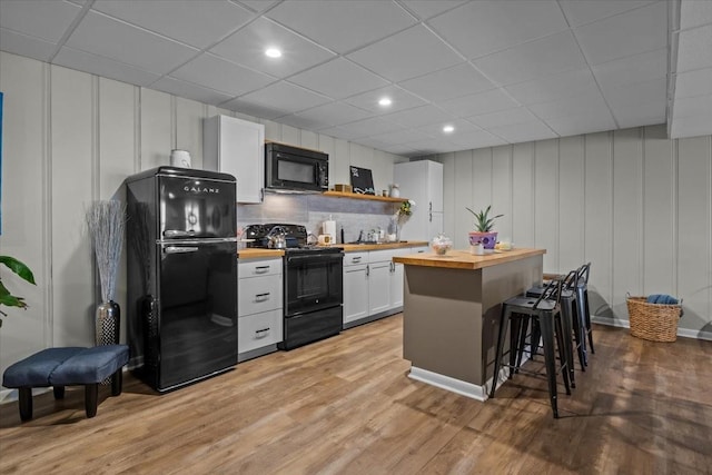 kitchen featuring open shelves, light wood-style flooring, black appliances, wood counters, and a kitchen bar