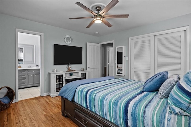 bedroom featuring a ceiling fan, baseboards, a closet, light wood finished floors, and ensuite bath