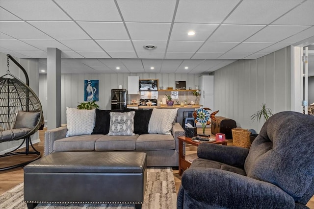 living area with light wood finished floors, visible vents, and a drop ceiling