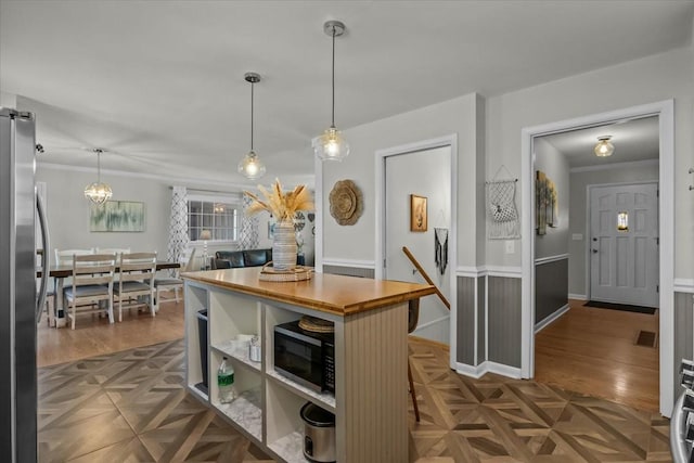 kitchen featuring black microwave, butcher block countertops, parquet flooring, freestanding refrigerator, and pendant lighting