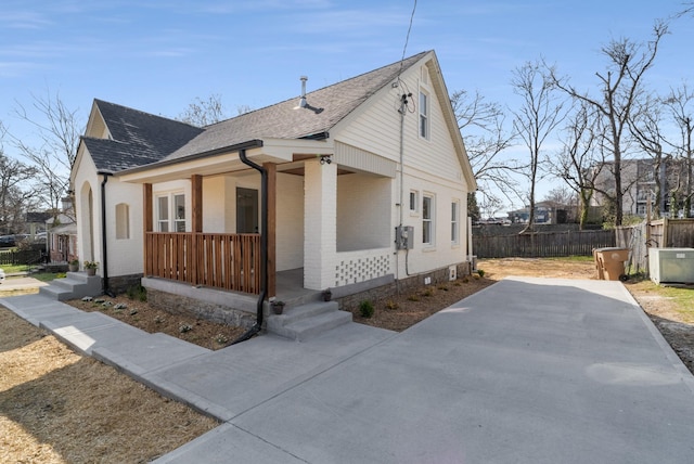 view of front of house featuring roof with shingles, covered porch, brick siding, and fence