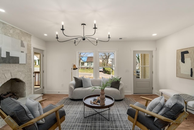 living room with a notable chandelier, wood finished floors, recessed lighting, a stone fireplace, and baseboards