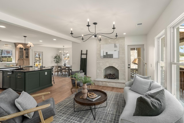 living area featuring visible vents, recessed lighting, a fireplace, a notable chandelier, and light wood-type flooring