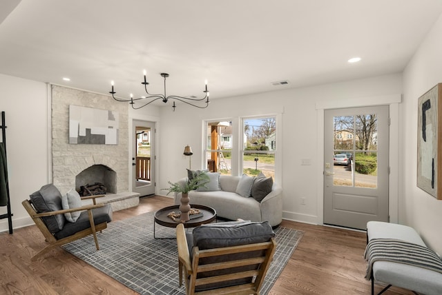 living room with a stone fireplace, a healthy amount of sunlight, wood finished floors, and a chandelier