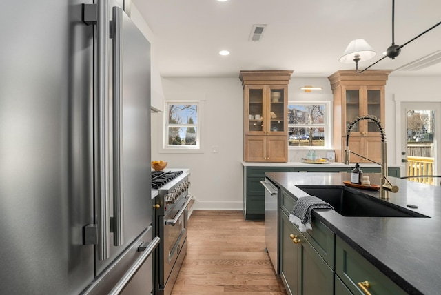 kitchen with a healthy amount of sunlight, visible vents, premium appliances, a sink, and light wood-type flooring