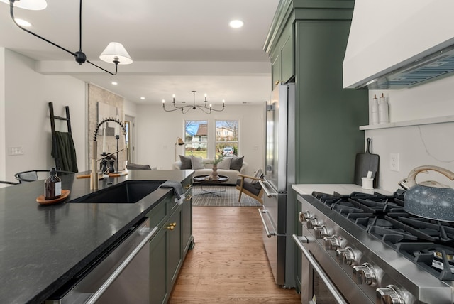 kitchen with green cabinets, light wood-style floors, exhaust hood, a notable chandelier, and stainless steel appliances