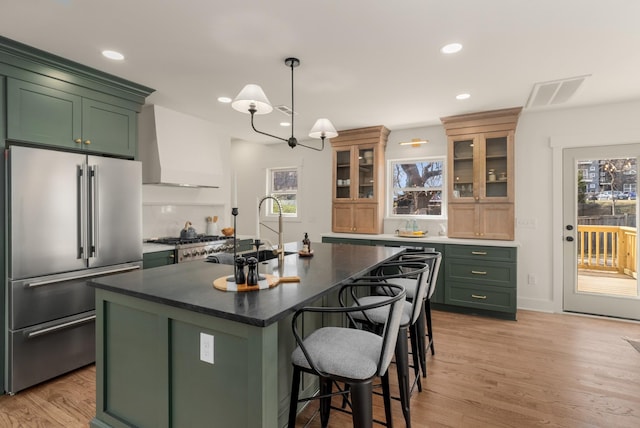 kitchen featuring premium range hood, light wood-style flooring, a sink, high end refrigerator, and green cabinets