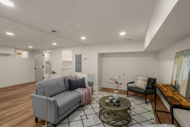 living area featuring electric panel, visible vents, baseboards, and light wood-style floors