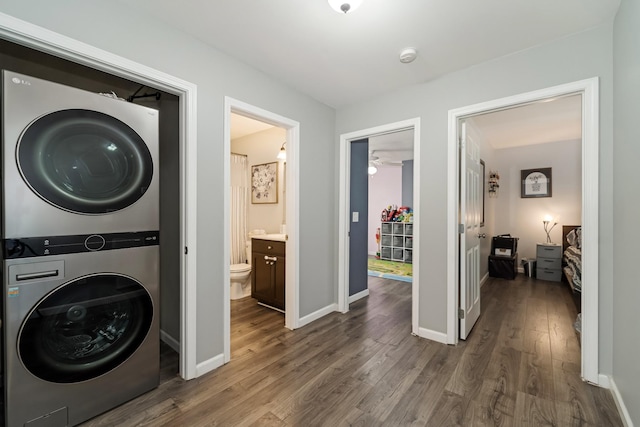 washroom with stacked washer / drying machine, baseboards, wood finished floors, and laundry area