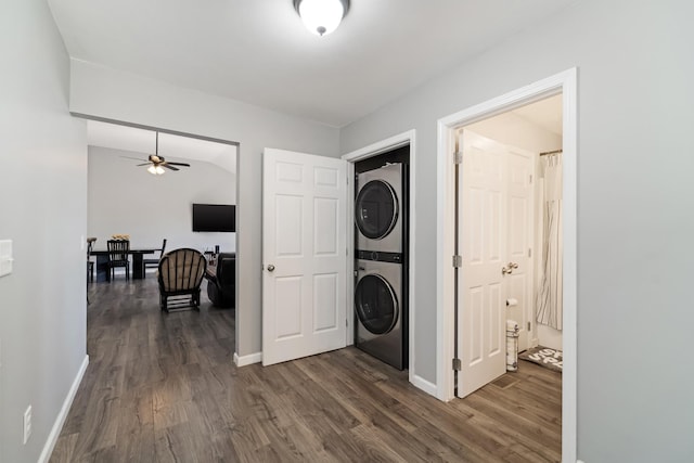 laundry room with baseboards, stacked washer and dryer, and dark wood finished floors