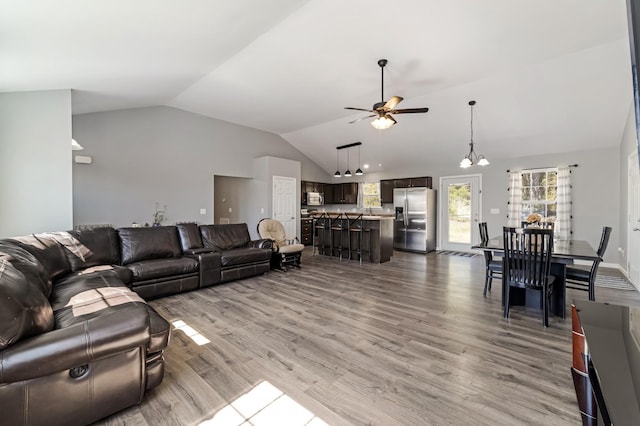 living room featuring ceiling fan with notable chandelier, wood finished floors, and vaulted ceiling