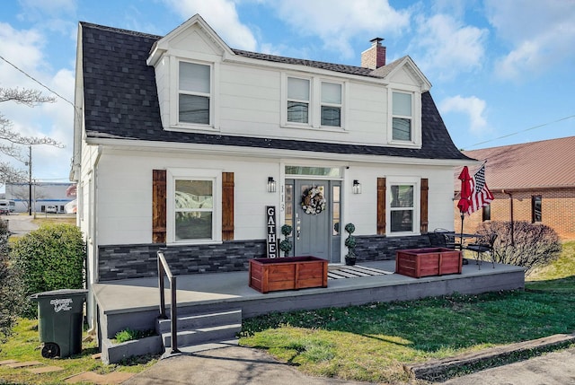 colonial inspired home with stone siding, roof with shingles, and a chimney