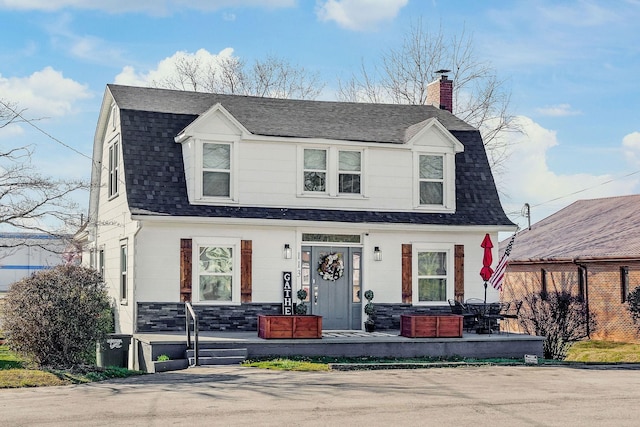 dutch colonial featuring a chimney, a gambrel roof, and roof with shingles