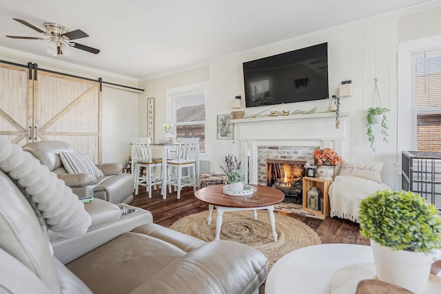 living room featuring ceiling fan, a barn door, wood finished floors, a brick fireplace, and crown molding