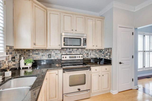 kitchen with crown molding, appliances with stainless steel finishes, cream cabinetry, light wood finished floors, and tasteful backsplash