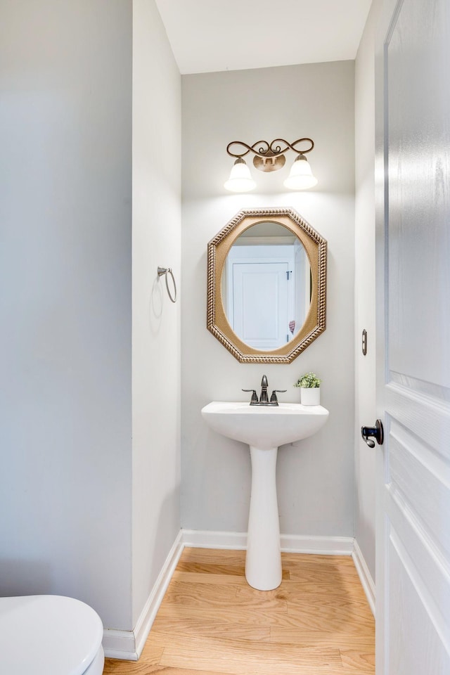 half bathroom featuring wood finished floors, toilet, and baseboards