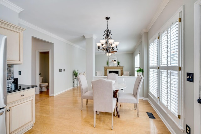 dining area with a fireplace, a notable chandelier, light wood finished floors, visible vents, and ornamental molding